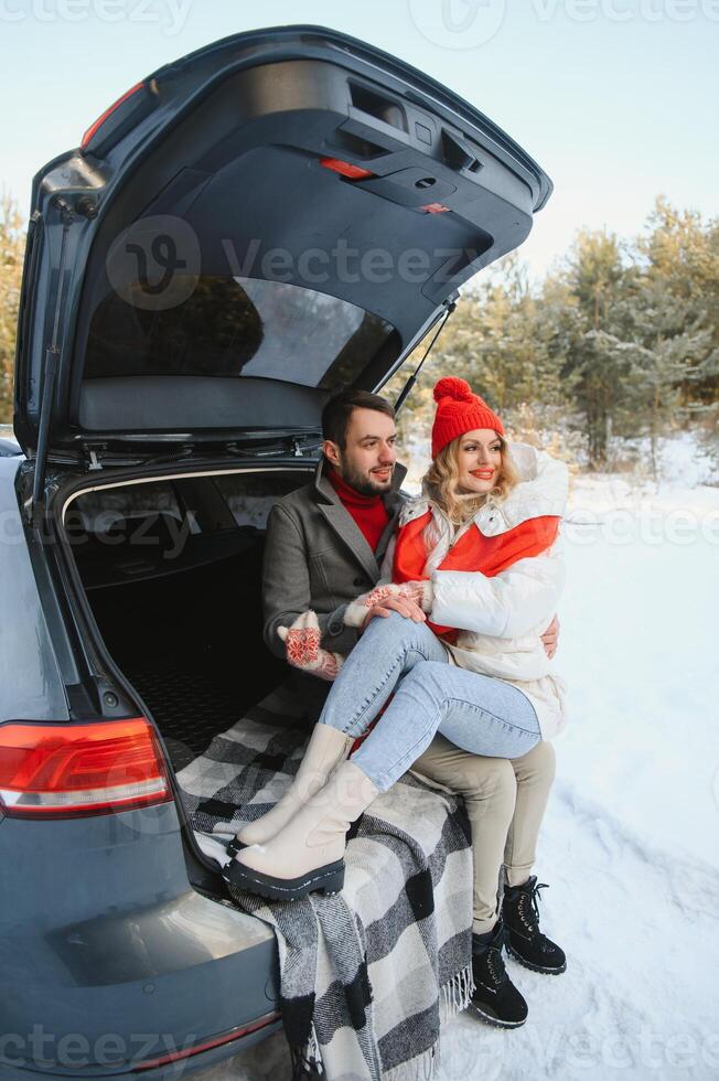 Happy couple sitting in open car back, having stop off. Romantic traveling concept. Winter forest. photo