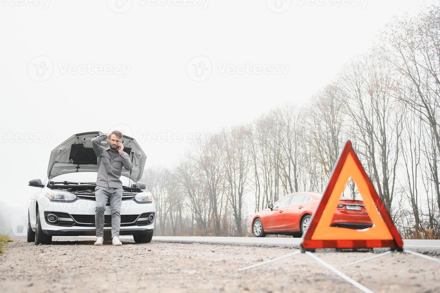 Sad driver calling car service, opening hood, having engine problem standing near broken car on the road. Car breakdown concept photo