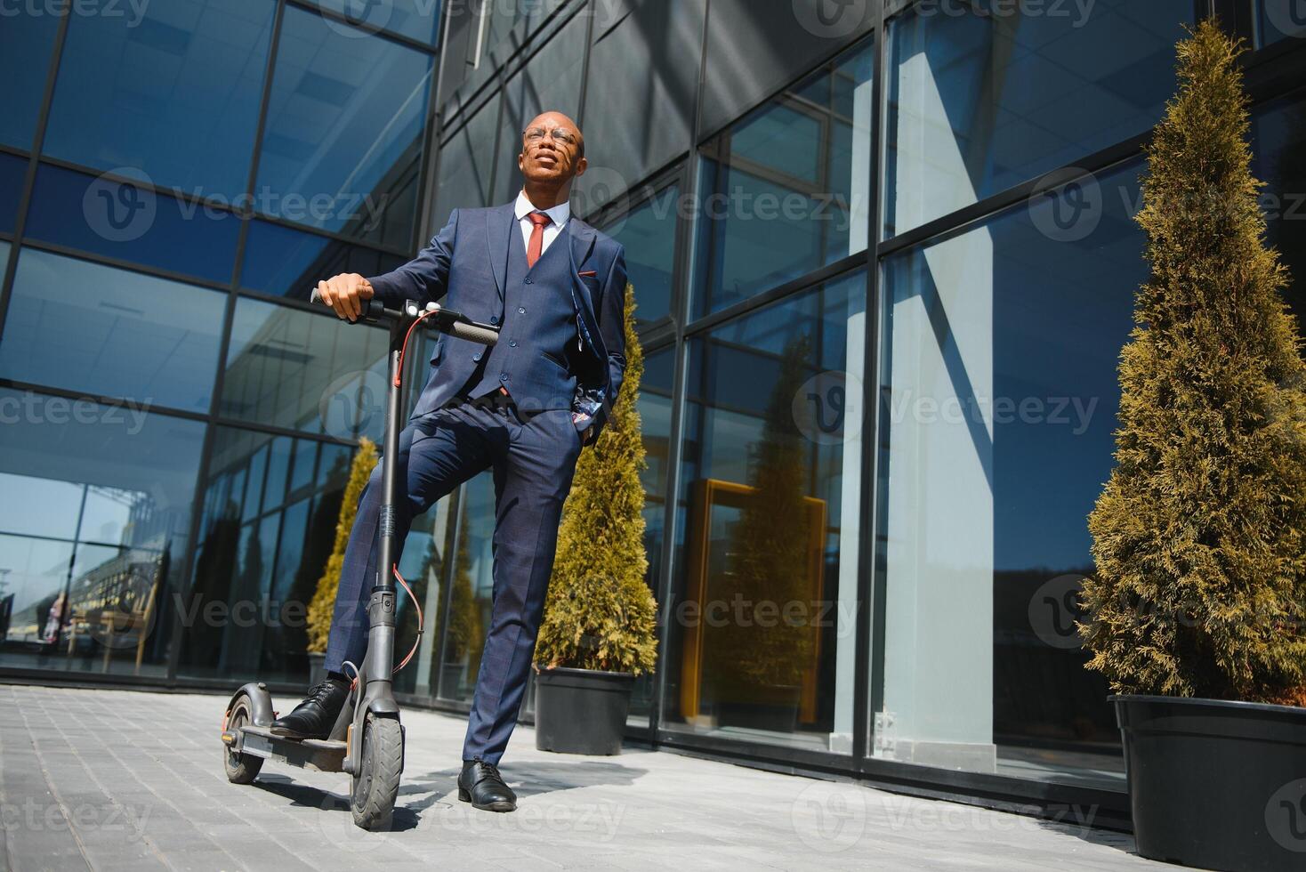 Handsome african 30s man wearing coat smiling while riding electric scooter outdoors photo