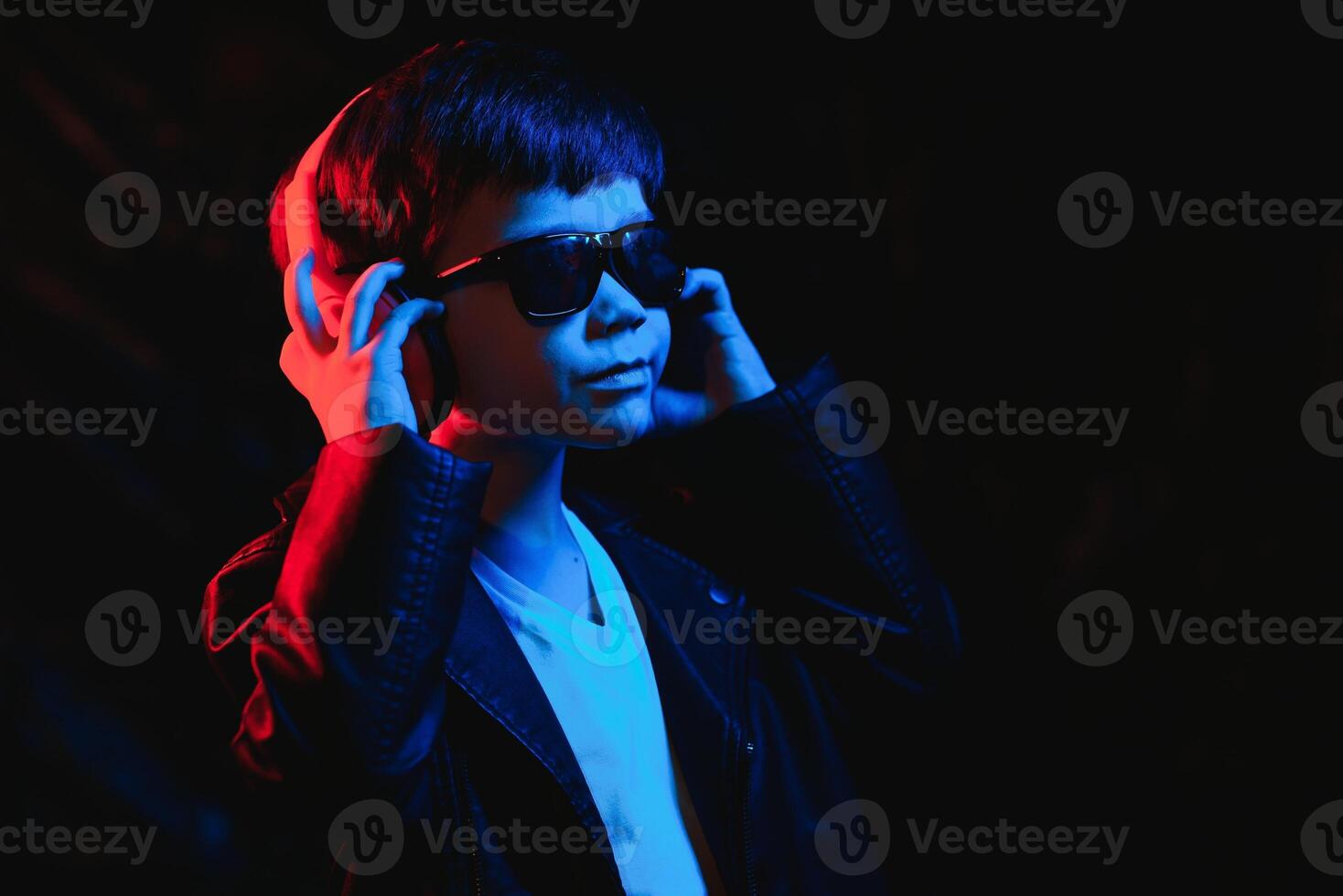 Studio shot in dark studio with neon light. Portrait of a stylish boy with headphones photo