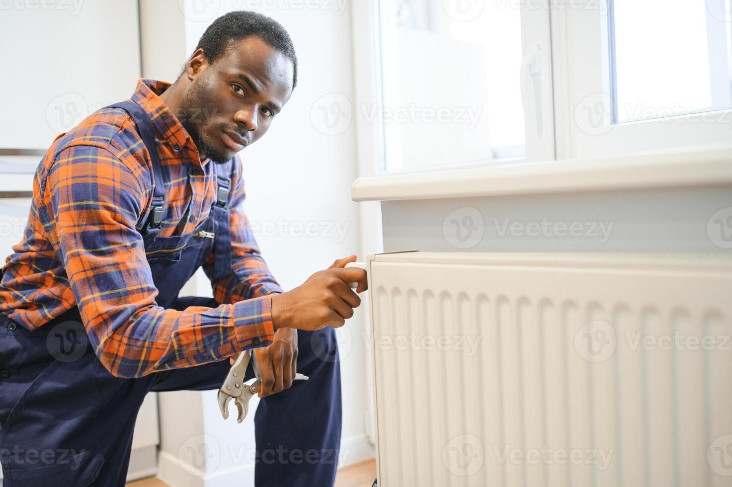 Repair heating radiator close-up. African man repairing radiator with wrench. Removing air from the radiator photo