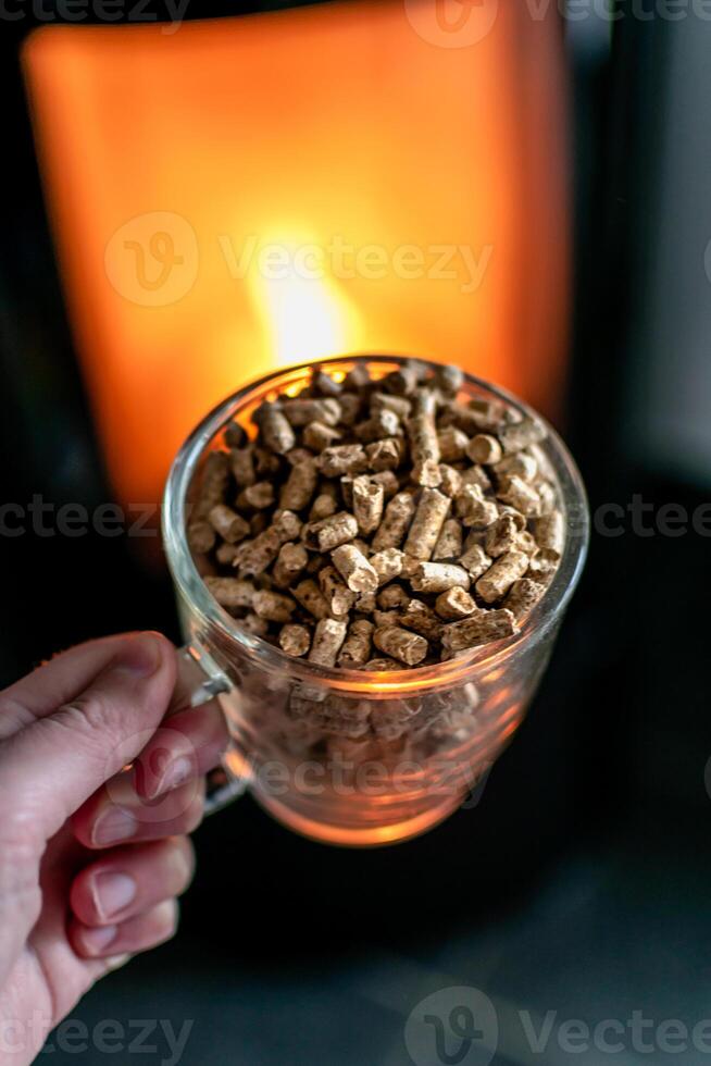 Pellet for stove or boiler in a glass, compressed wood pellet with a stove in background photo