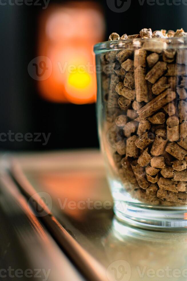 Pellet for stove or boiler in a glass, compressed wood pellet with a stove in background photo