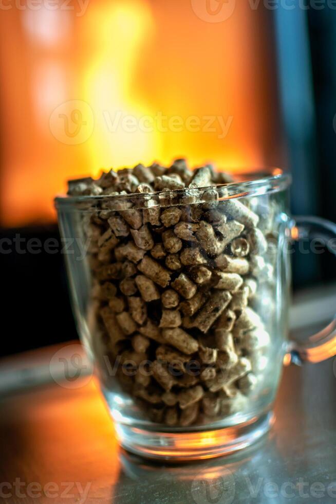 Pellet for stove or boiler in a glass, compressed wood pellet with a stove in background photo
