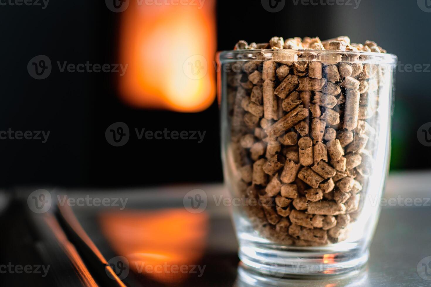 Pellet for stove or boiler in a glass, compressed wood pellet with a stove in background photo