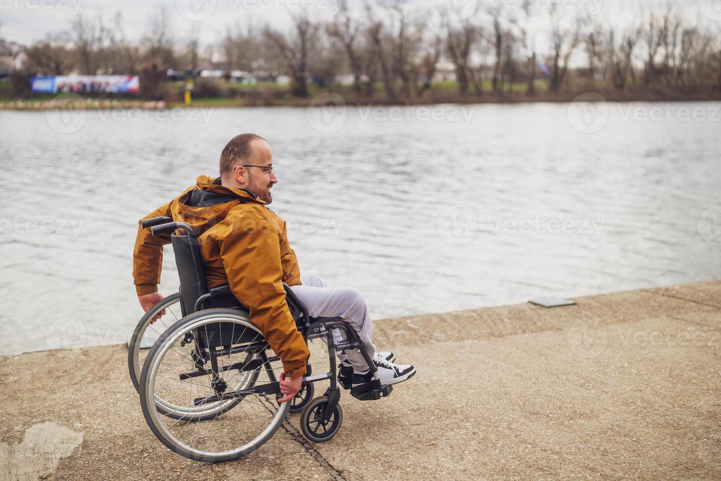 Happy paraplegic handicapped man in wheelchair by the lake. He is rolling on walkway. photo