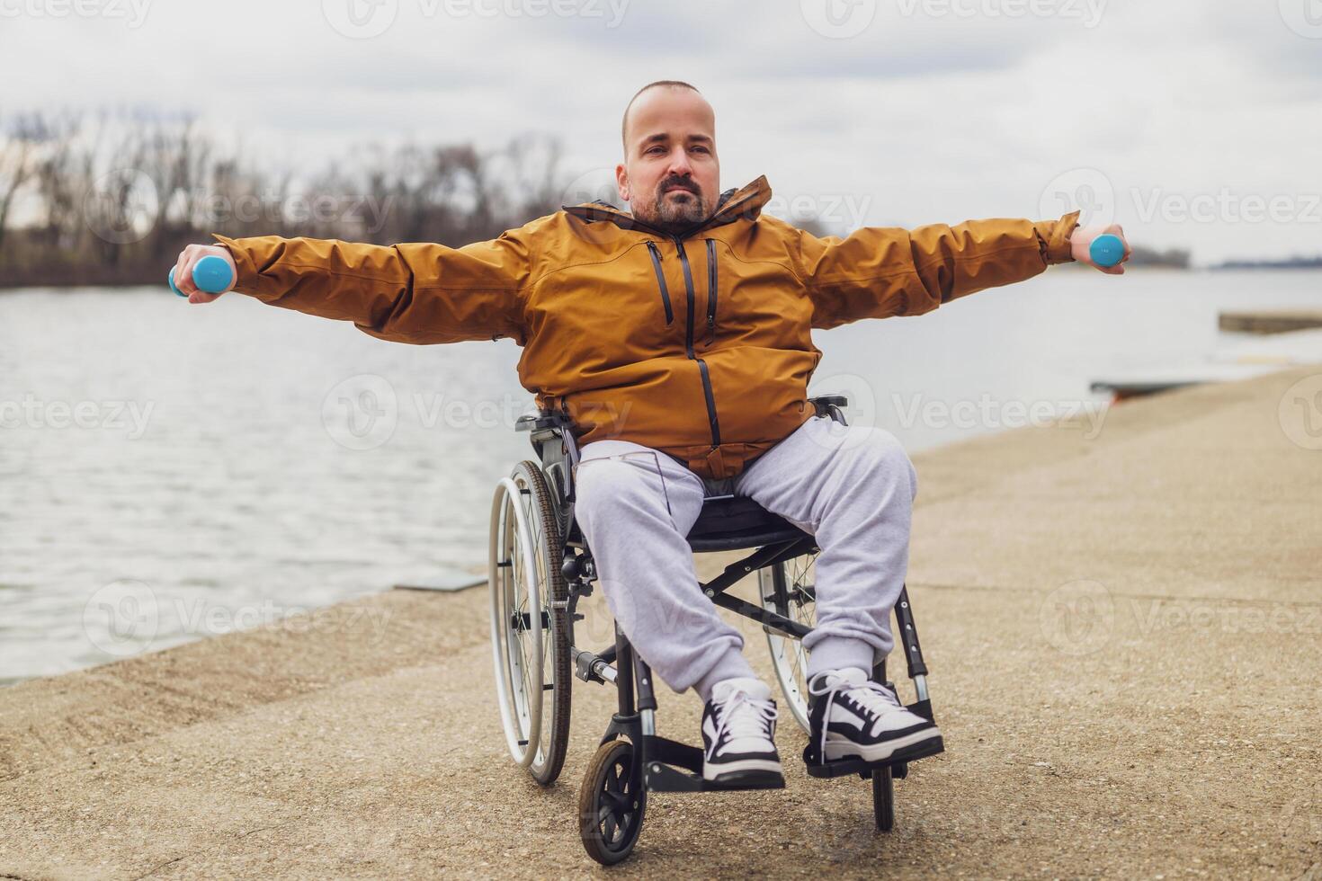 Paraplegic handicapped man in wheelchair by the lake. He is exercising with weights. photo