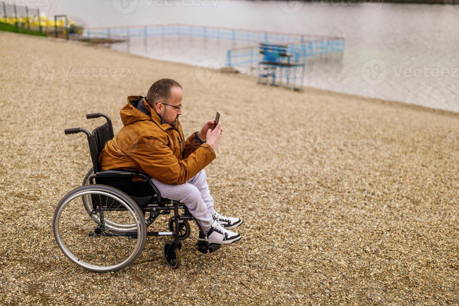 parapléjico minusválido hombre en silla de ruedas es mensajería en teléfono inteligente exterior. foto