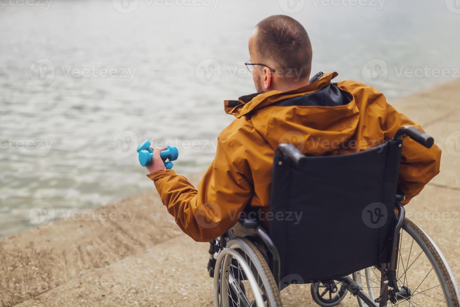 Paraplegic handicapped man in wheelchair by the lake. He is ready for exercise with weights. photo