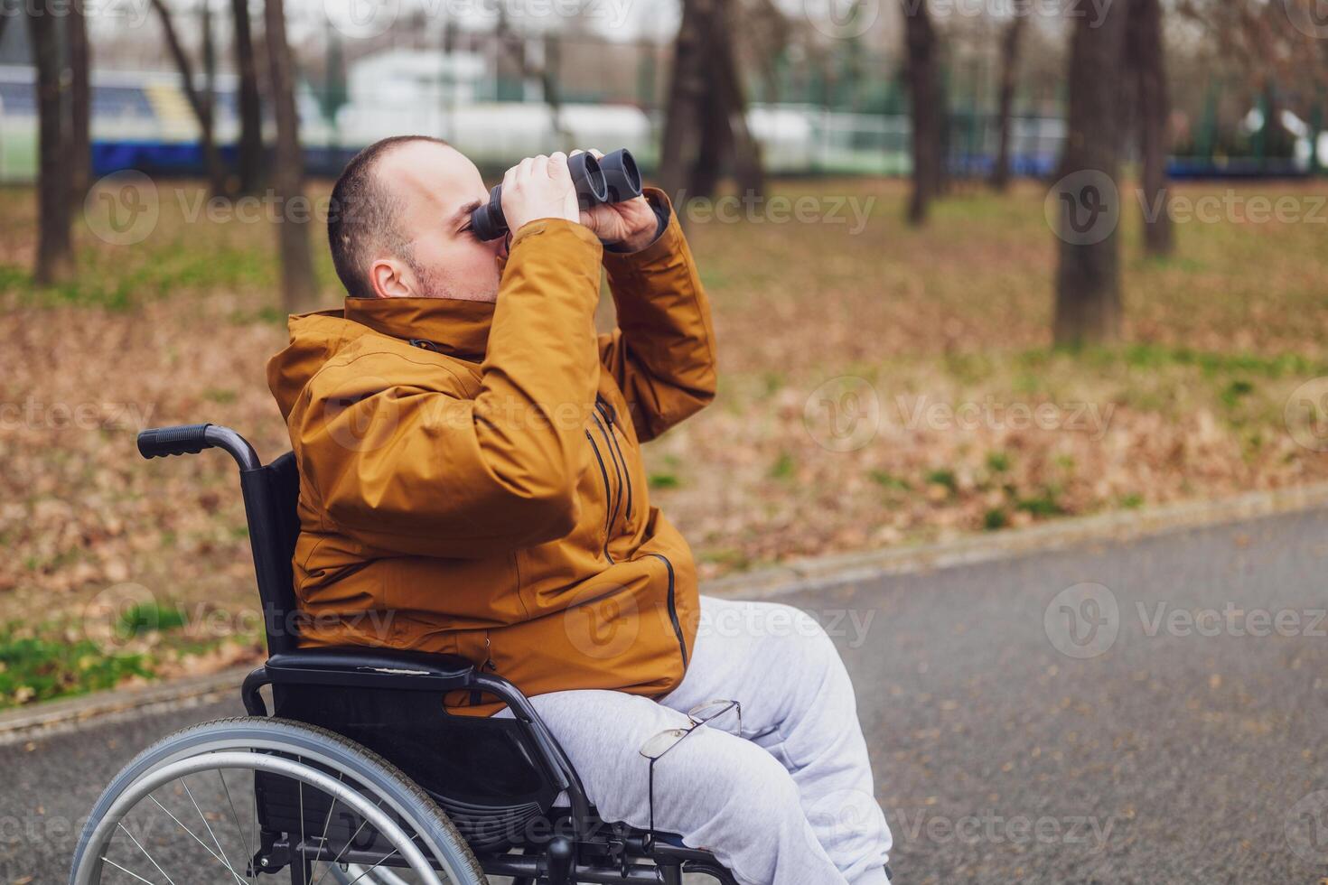 parapléjico minusválido hombre en silla de ruedas es utilizando prismáticos exterior. él es acecho aves. foto