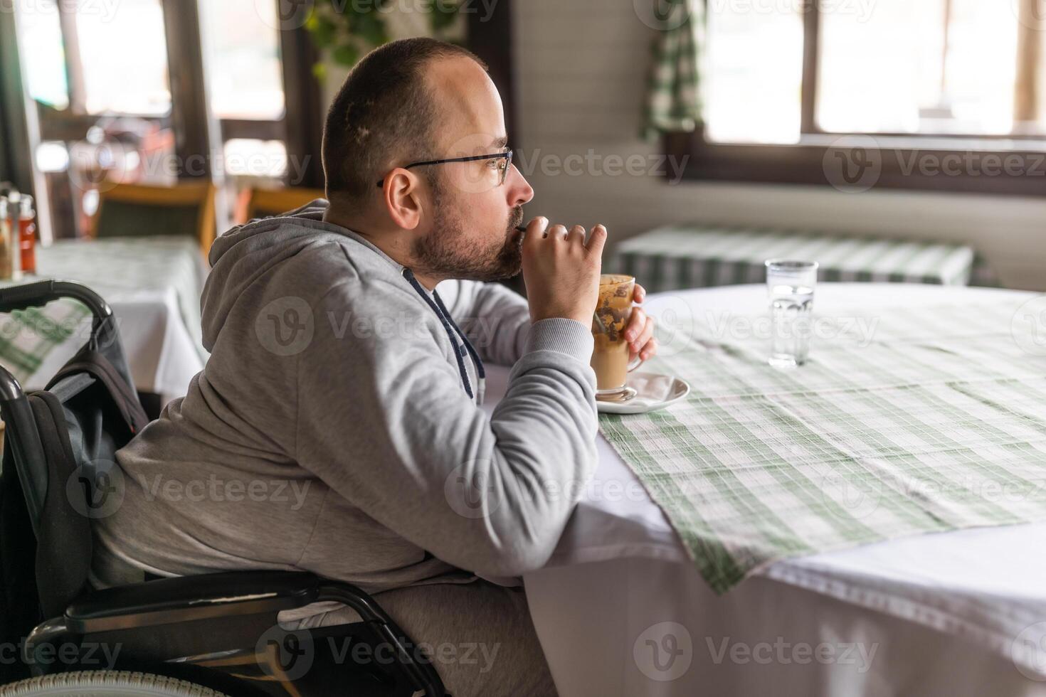 Paraplegic handicapped man in wheelchair is sitting at restaurant and drinking coffee. photo