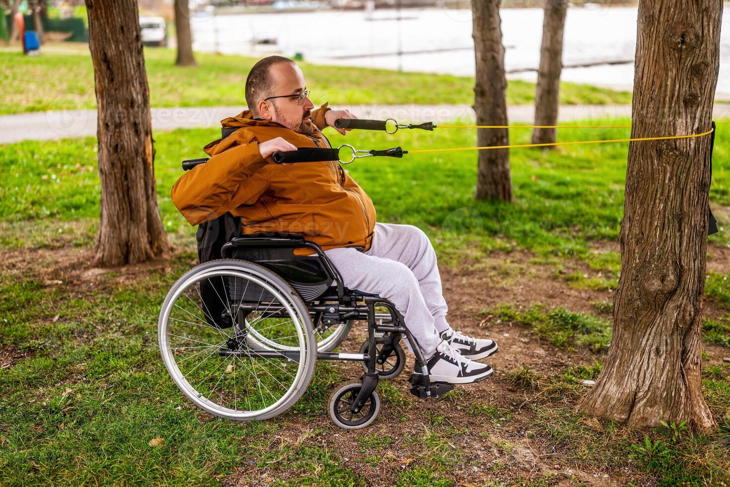 Paraplegic handicapped man in wheelchair is exercising with stretch band in park. photo