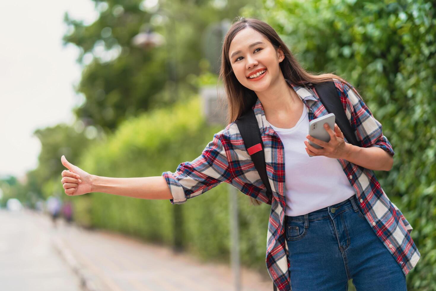 beautiful young woman with a backpack uses a phone while hailing a car to travel photo