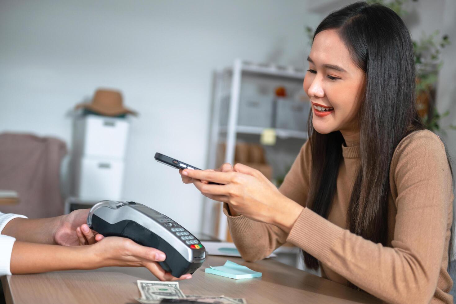 Young Asian woman smiling and paying with smartphone in restaurant photo