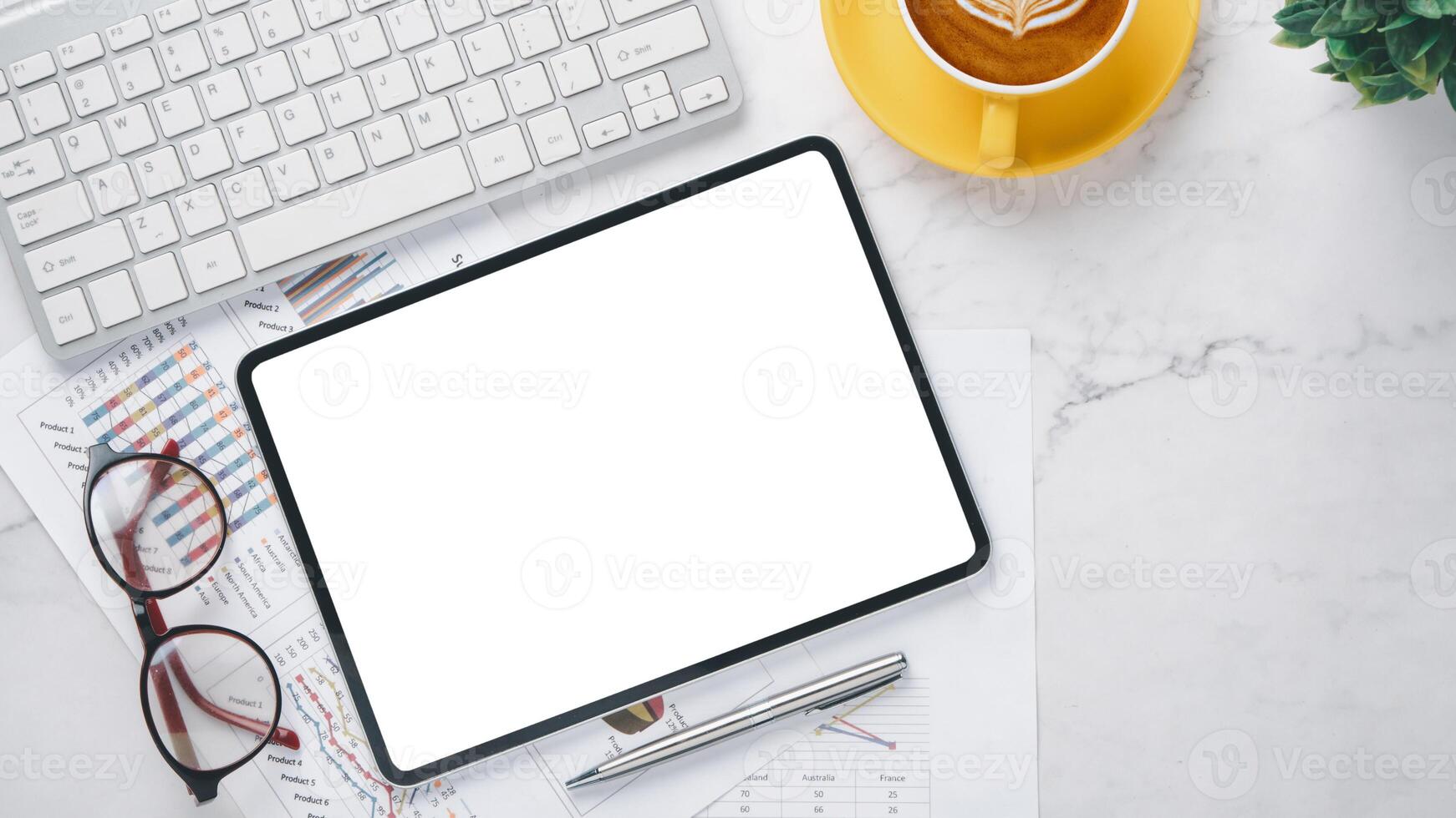 A blank tablet screen on a marble desk with a keyboard, coffee cup, glasses, and business charts, ready for productivity. photo