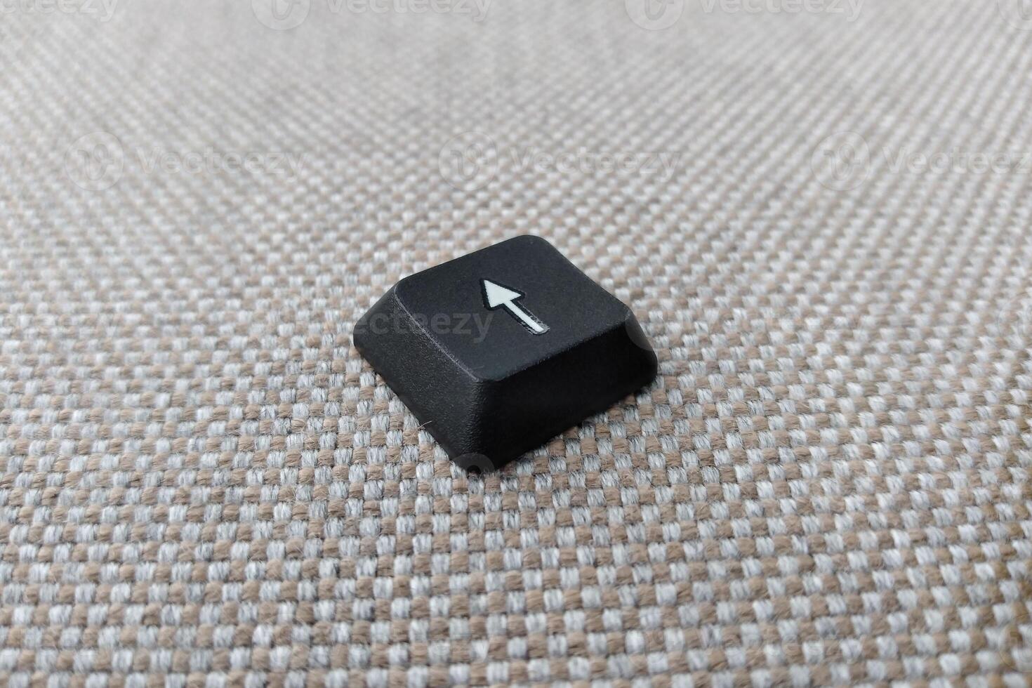 Keyboard with arrow pointing up on grey carpet background, selective focus photo