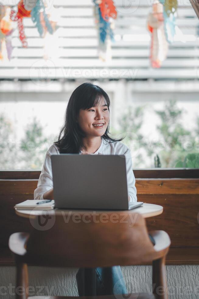 Freelance concept, A smiling woman is working on her laptop in a cafe decorated with colorful paper lanterns, enjoying a bright day. photo