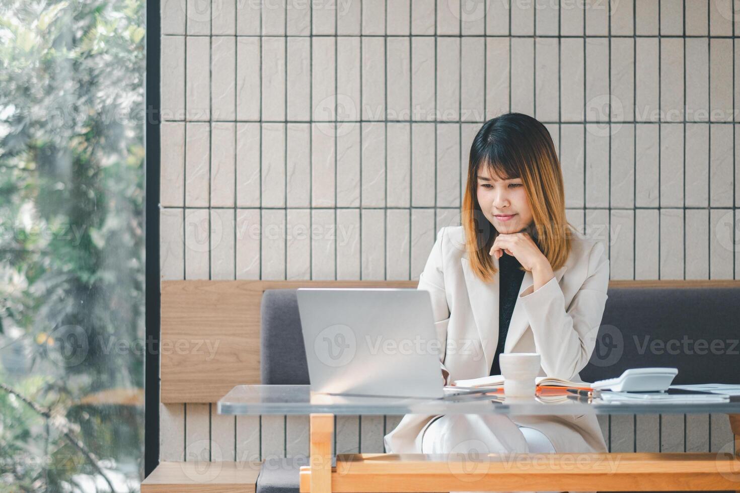 A pensive businesswoman in deep thought while working on her laptop at a well-lit cafe, surrounded by her work materials. photo