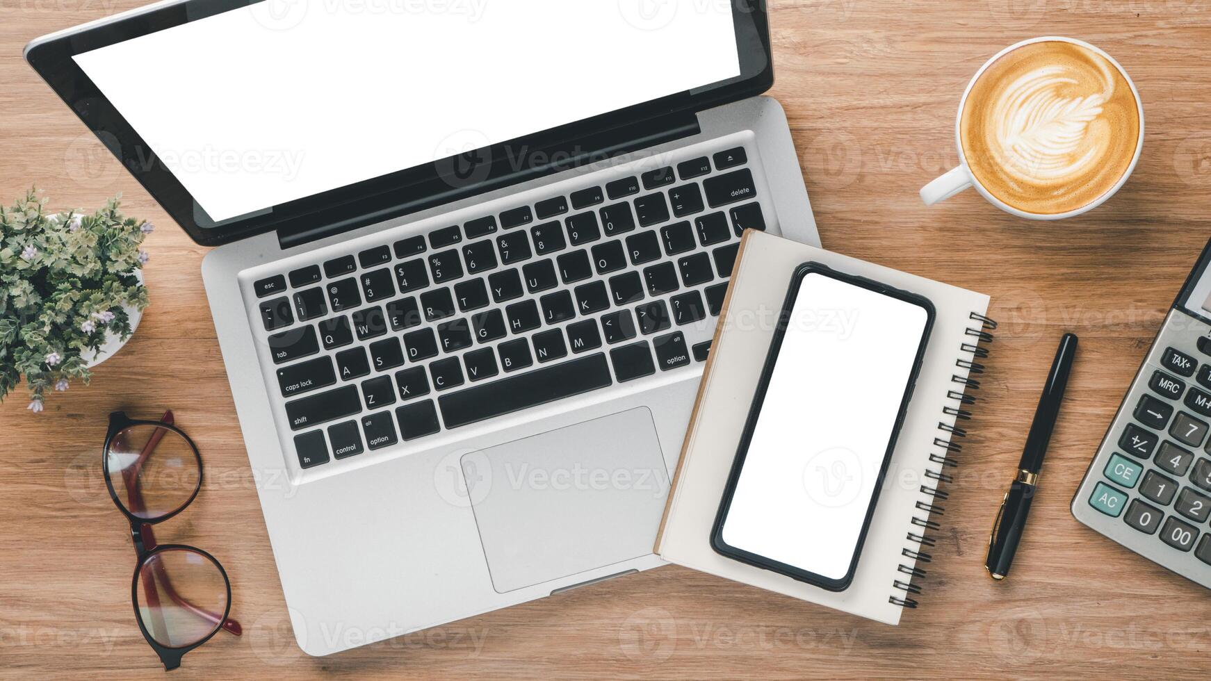 Top-down view of a well-arranged office desk featuring an open laptop, smartphone, notepad, and a cup of coffee with latte art. photo