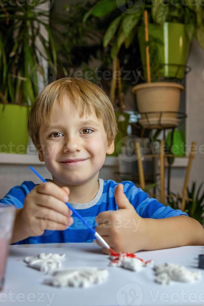 The kid draws and paints plaster figures with a brush and gouache on a piece of paper. photo