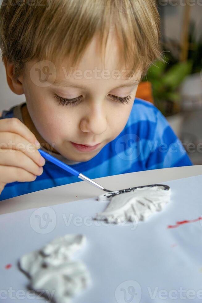 The kid draws and paints plaster figures with a brush and gouache on a piece of paper. photo