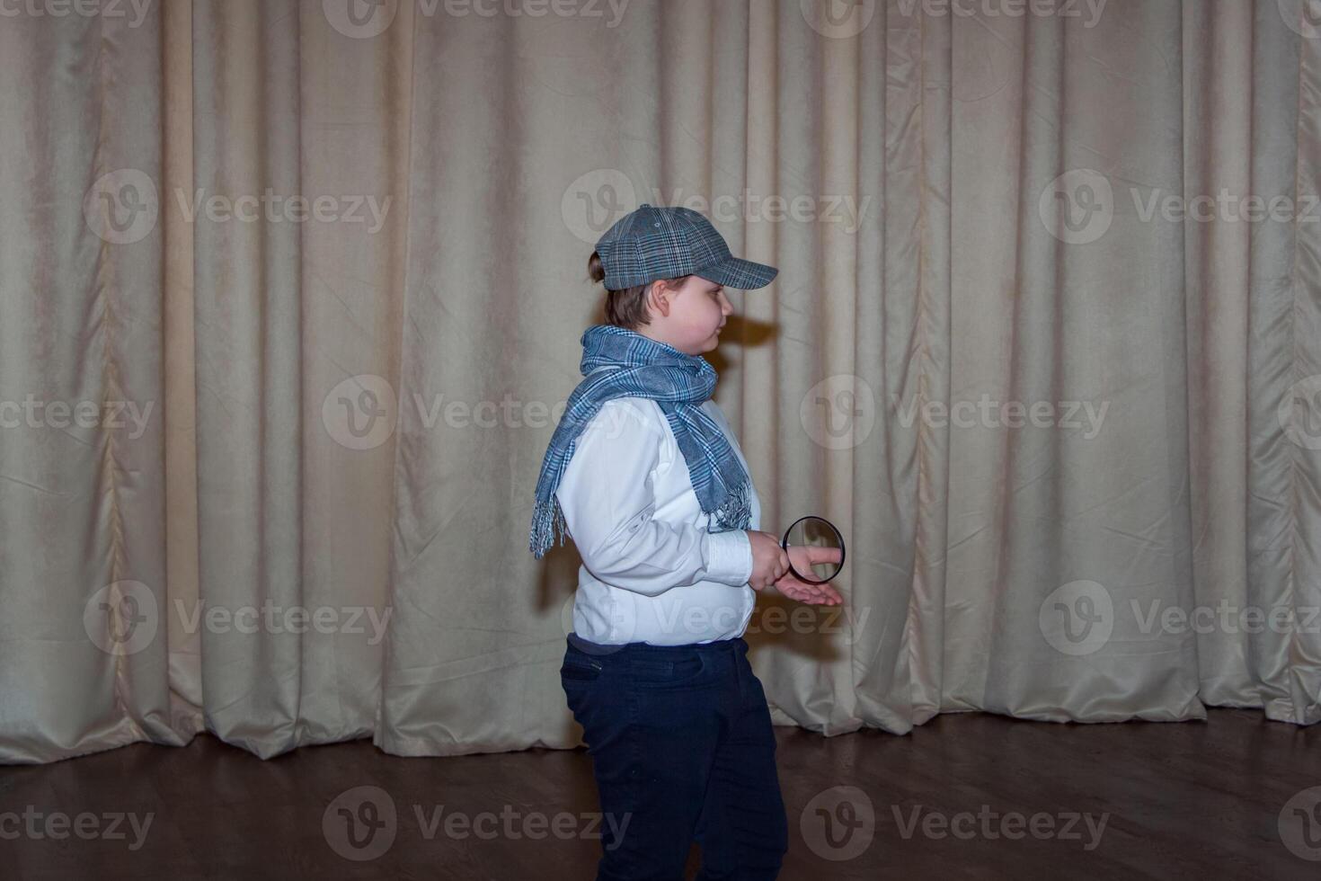 A cute teenage boy in a cap and a plaid scarf. The image of a detective. Magnifying glass in hand. photo