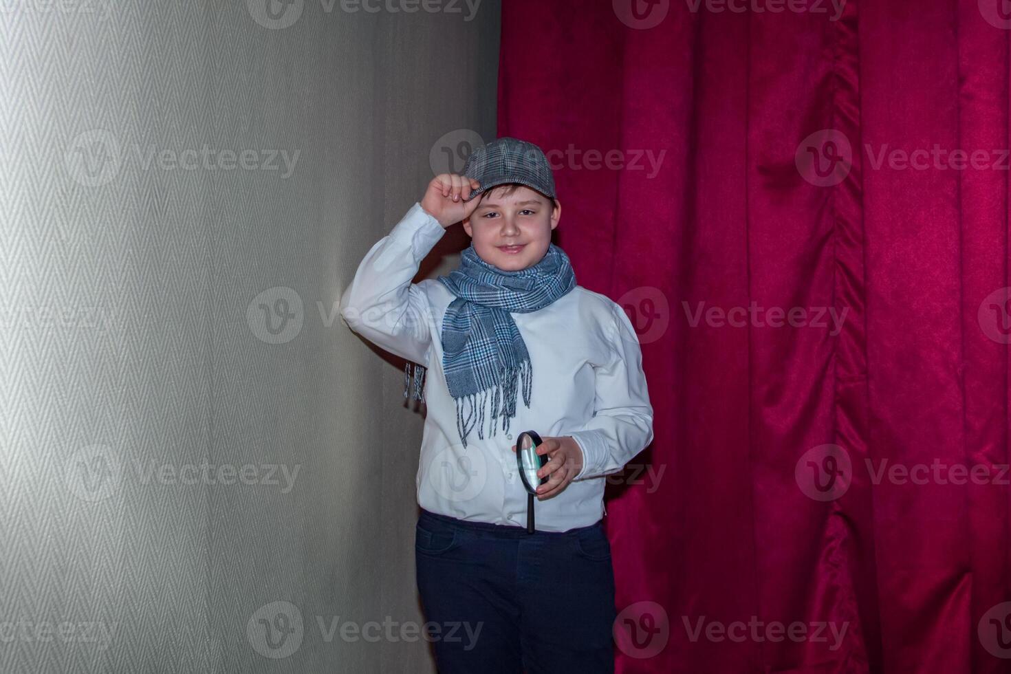 un linda Adolescente chico en un gorra y un tartán bufanda. el imagen de un detective. aumentador vaso en mano. foto