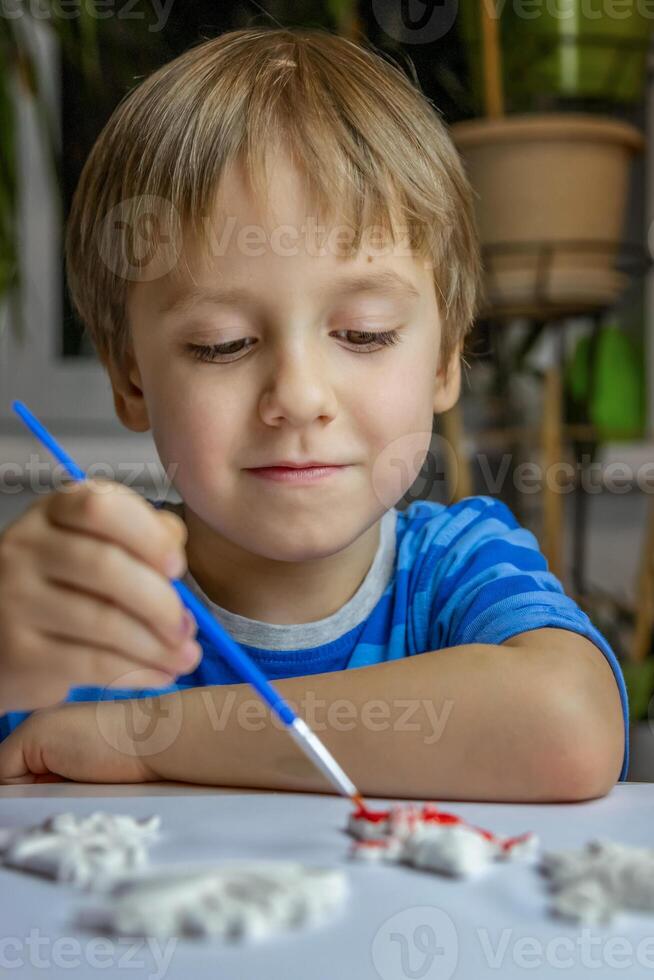 The kid draws and paints plaster figures with a brush and gouache on a piece of paper. photo