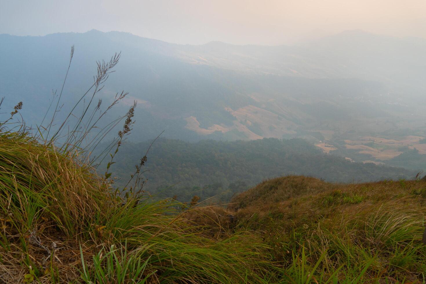 The foreground is covered with grass. Landscape view of mountain ranges lined up background. Under fog covers the sky. At Phu Langka Phayao Province of Thailand. photo