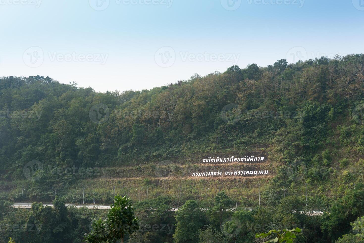 Landscape view of mountain at Khao Plung Rest Stop Uttaradit Thailand. Road cuts through the mountains. And the Thai text means welcome. under blue sky. photo