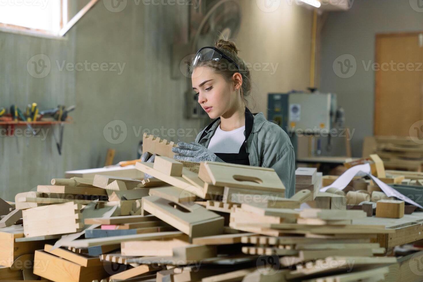 A young woman is training to be a carpenter in the workshop. She works with a laptop computer in a wood workshop. female carpenter contact customers by smartphone. SME orders, Start-ups and small photo