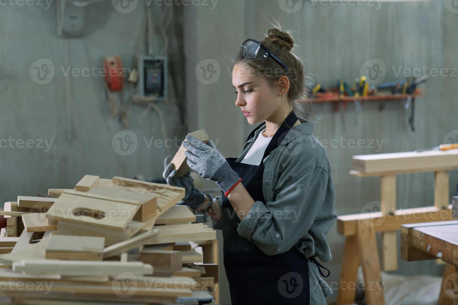 A young woman is training to be a carpenter in the workshop. She works with a laptop computer in a wood workshop. female carpenter contact customers by smartphone. SME orders, Start-ups and small photo