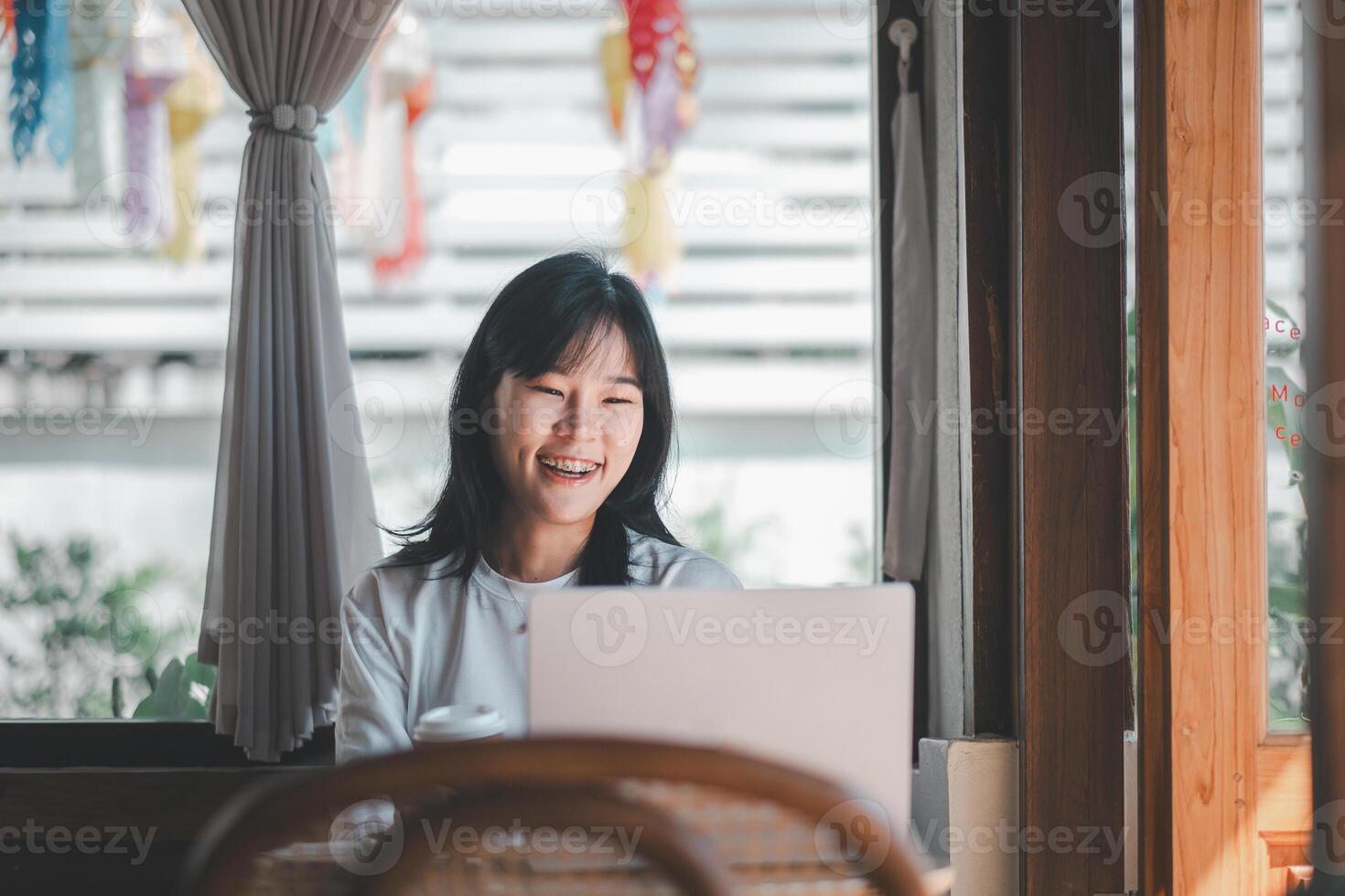 Business freelance concept, A joyful woman with braces smiles while working on her laptop in the warm ambiance of a sunny cafe interior. photo