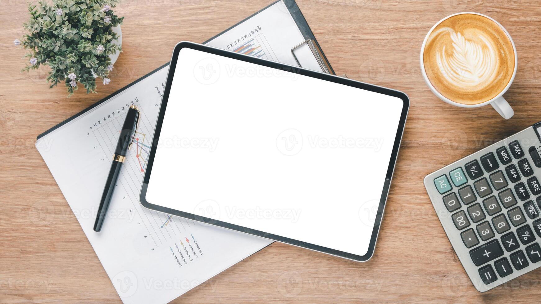 A professional workspace featuring a tablet with a blank screen, financial charts, pen, coffee, and calculator on a wooden table. photo