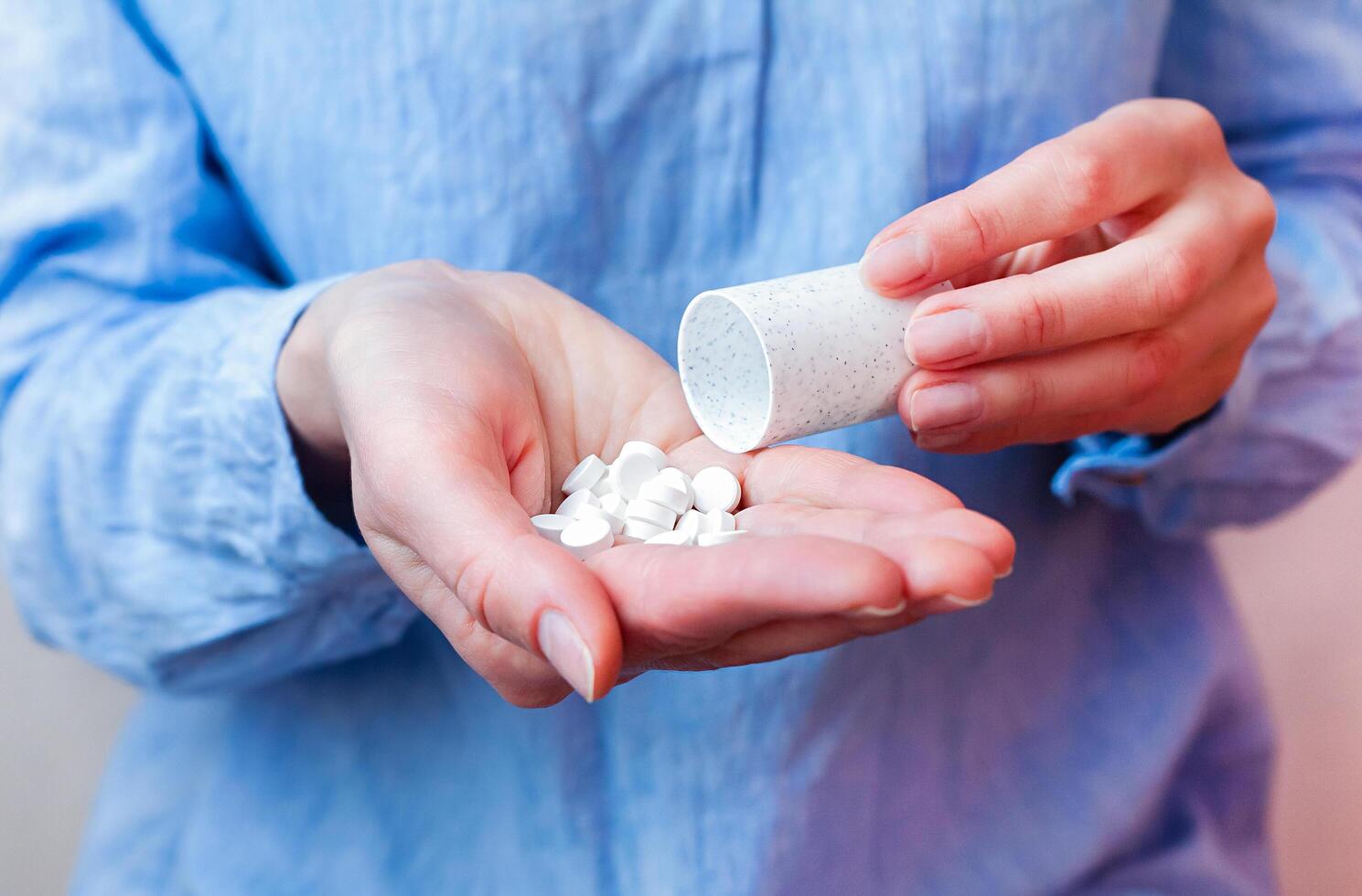 mujer en un azul blusa torrencial pastillas desde un botella dentro su mano. tomando antibiótico, antidepresivo y analgésico medicamento. de cerca. foto