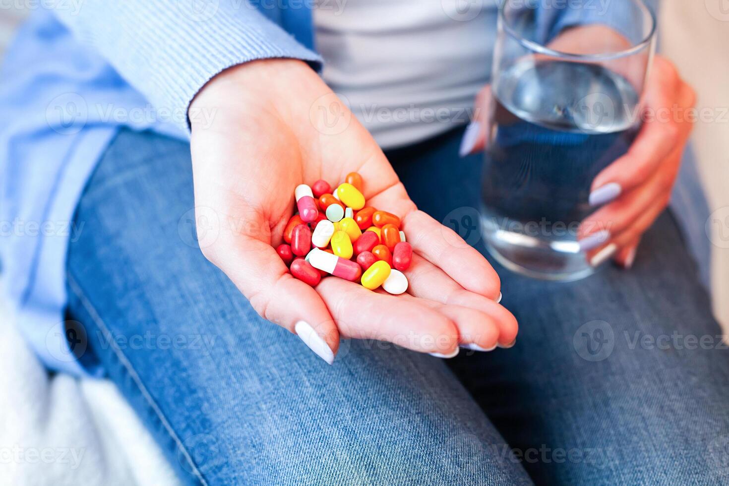 Woman holds multicolored pills and glass of water in hands. Taking supplements or antibiotic, vitamins, antidepressant, painkiller medication. Close-up. photo