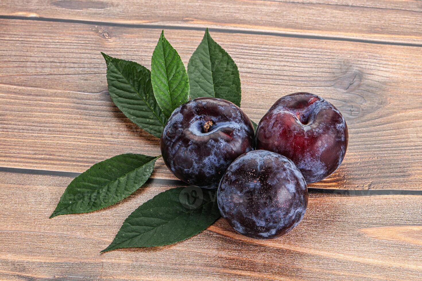 Raw purple plums heap with leaves photo