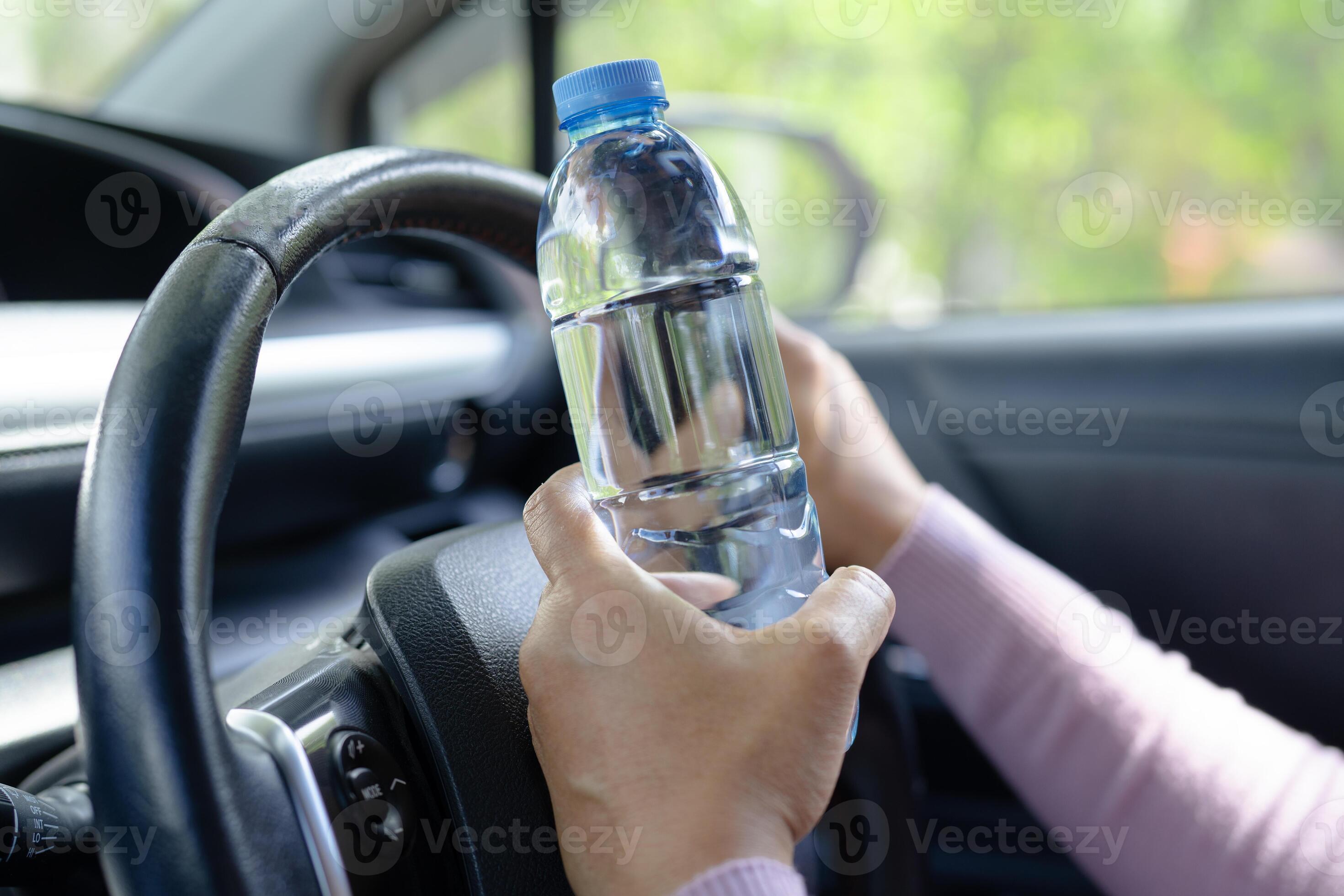 Asian woman driver holding bottle for drink water while driving a car. Plastic hot water bottle