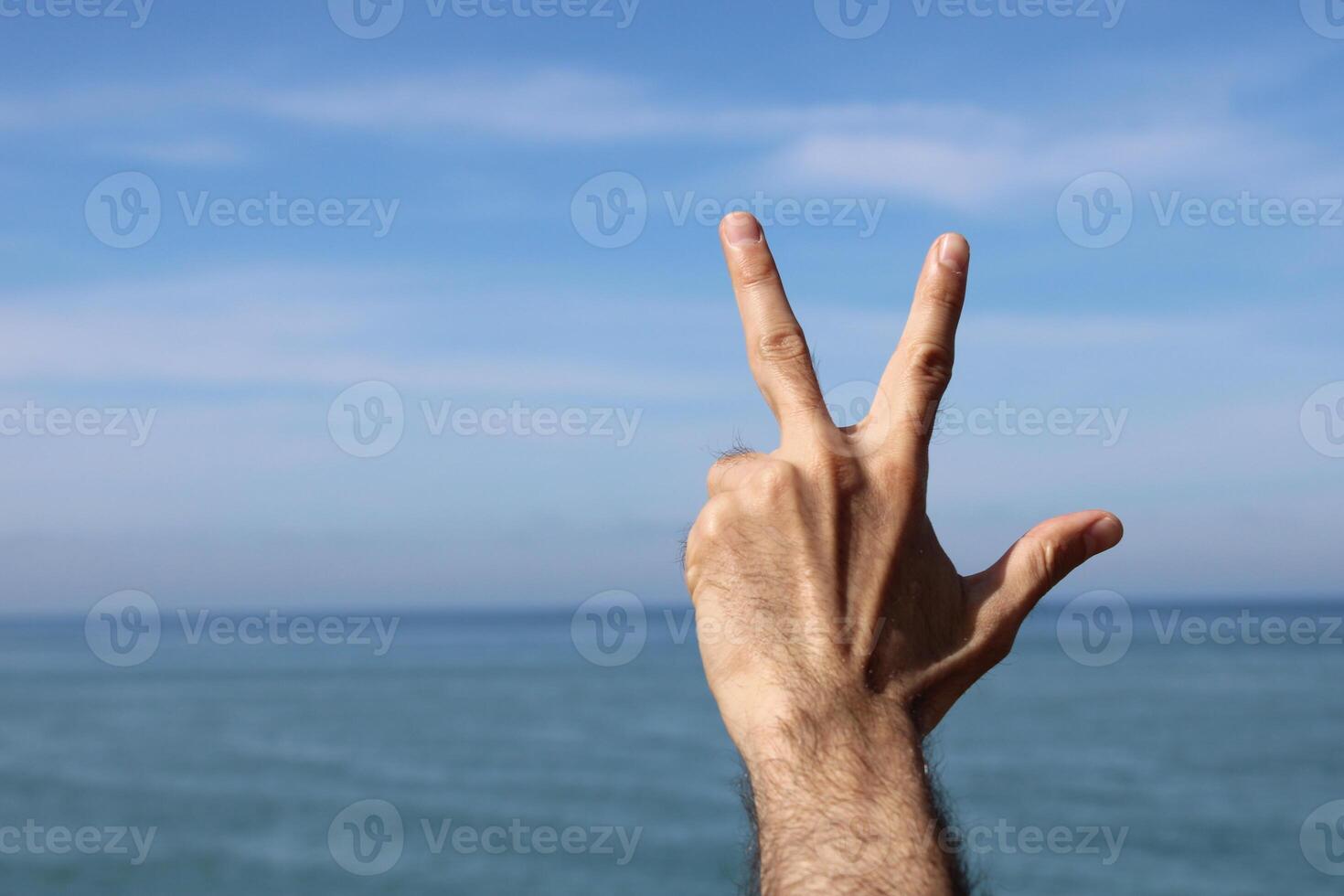 Hand doing,showing number three gesture symbol on blue summer sky nature background. Gesturing number 3. Number three in sign language. photo