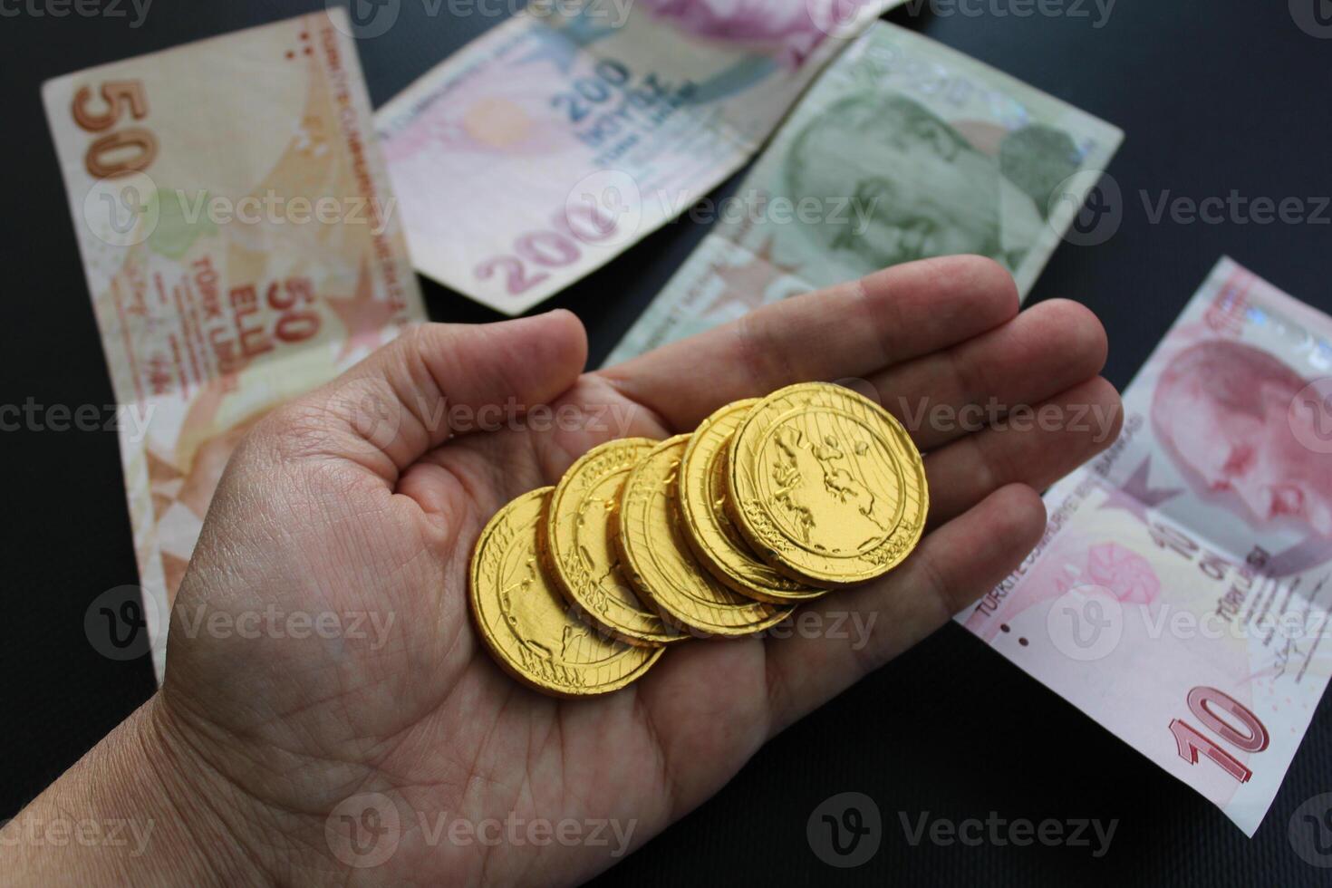 A hand holds a gold coin with the word dragon on it. Turkish banknotes in the background photo