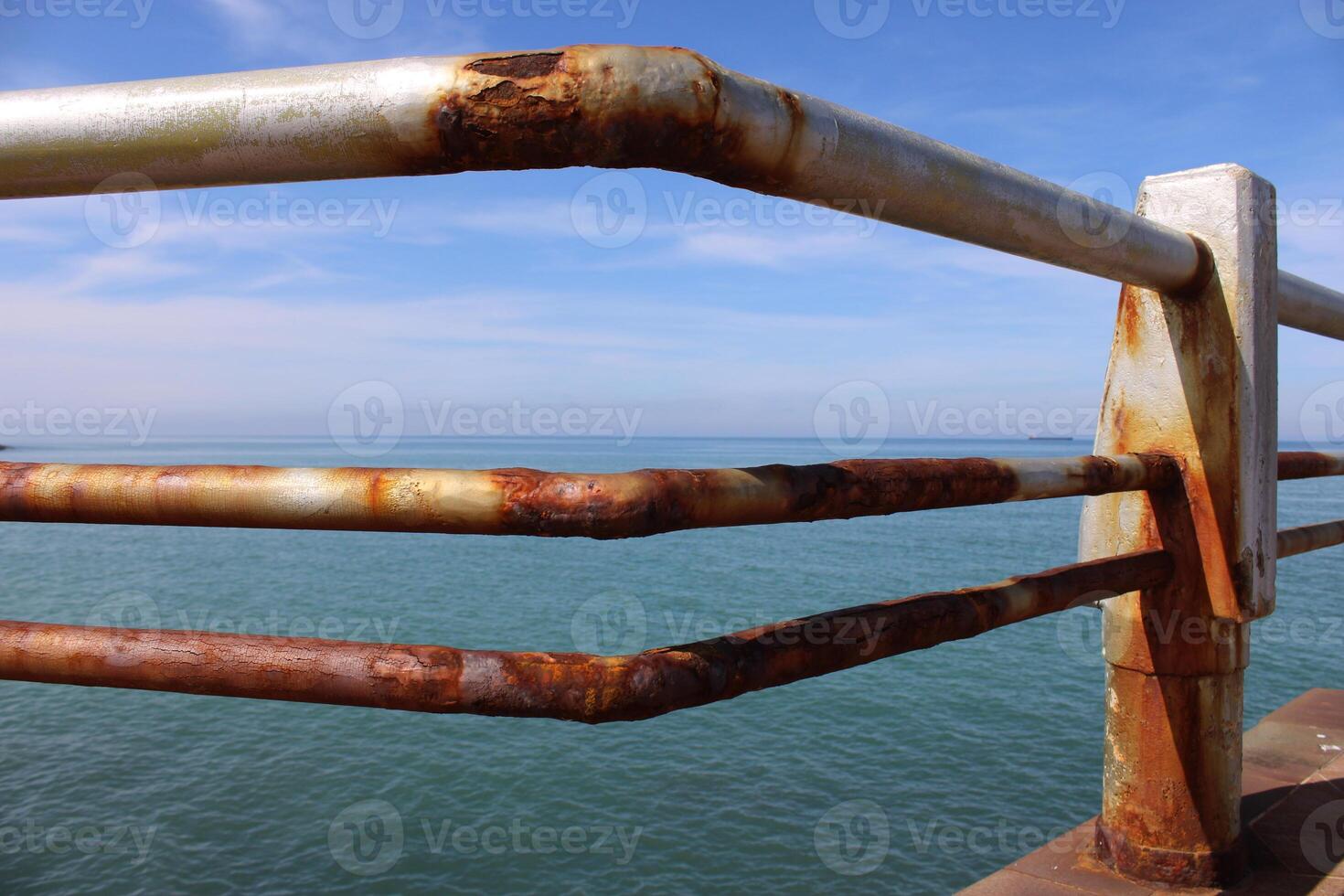 A rusty fence with a blue sea in the background.Rusty iron railing, beautiful sea and sky landscape view between rusty railing gap. photo