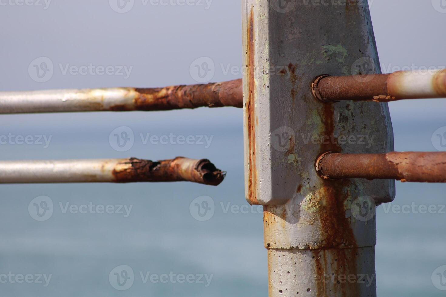 A rusty fence with a blue sea in the background.Rusty iron railing, beautiful sea and sky landscape view between rusty railing gap. photo