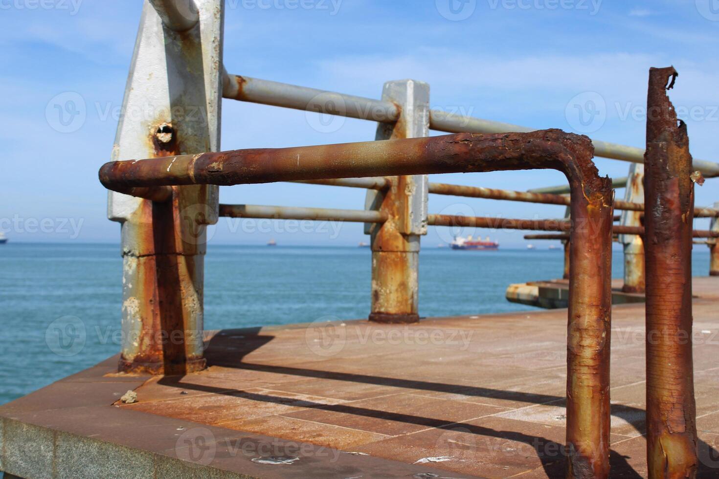 A rusty fence with a blue sea in the background.Rusty iron railing, beautiful sea and sky landscape view between rusty railing gap. photo