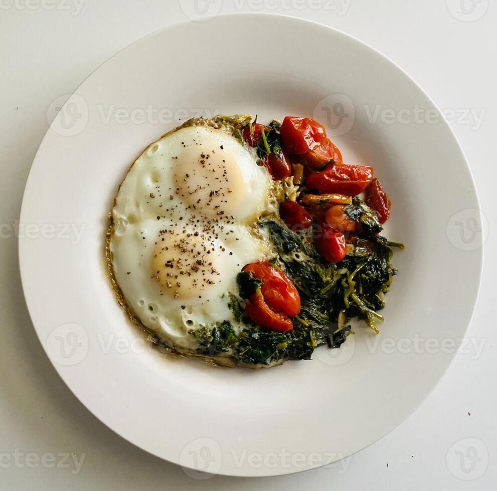 fried eggs with spinach and cherry tomatoes on a white plate, top view photo