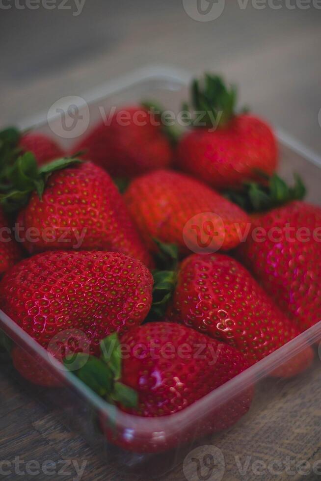 Strawberries in a plastic box on a wooden table. Selective focus. photo