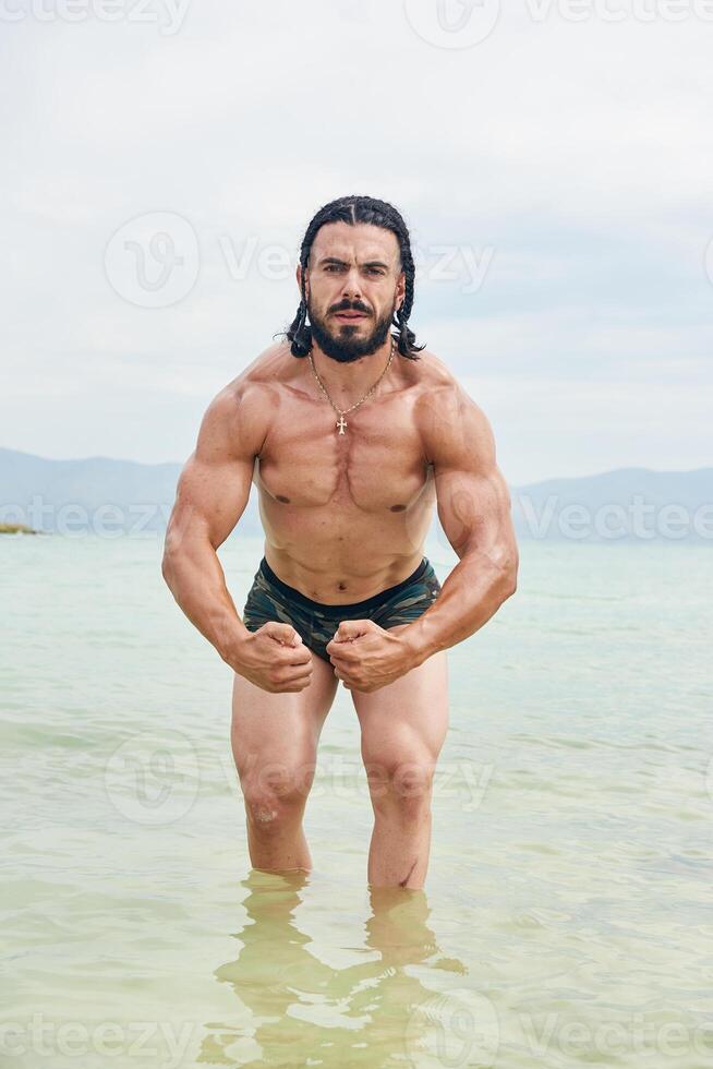 joven muscular hombre hacer ejercicio en el playa, joven muscular hombre haciendo culturismo ejercicios en el playa, atlético joven hombre en el playa foto