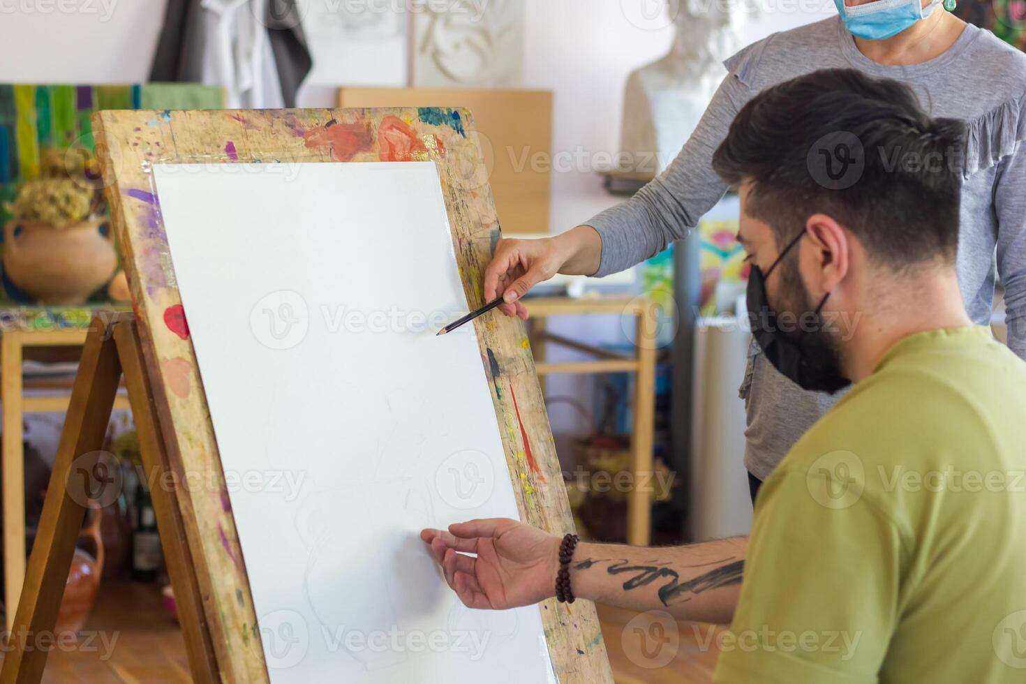 teacher helping student in art scholl, student with protective mask drawing picture photo