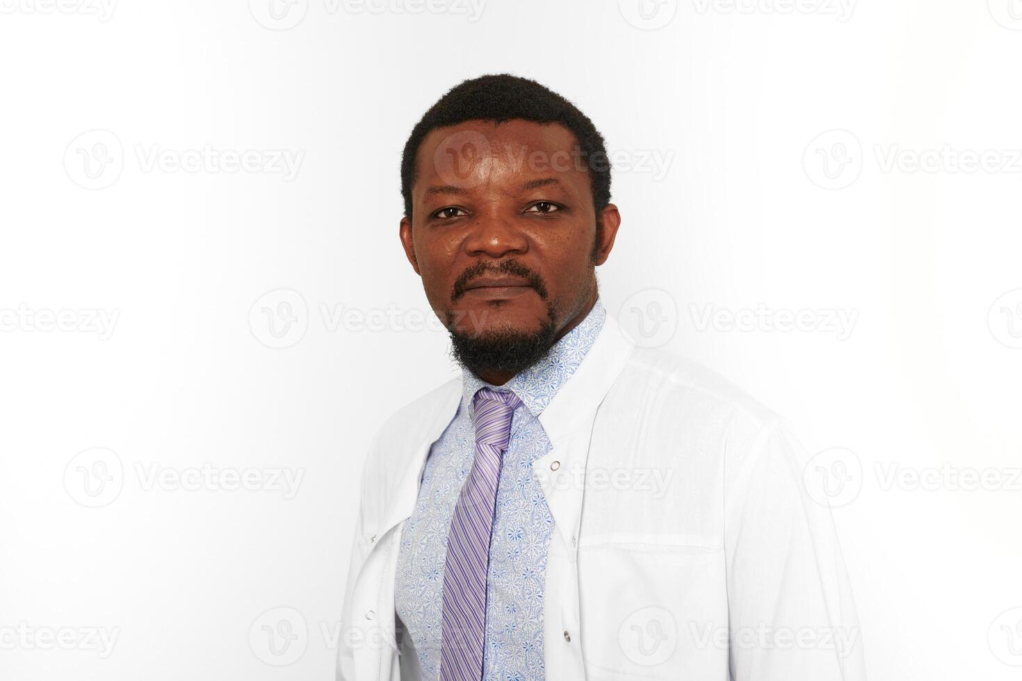 Serious black doctor man with small beard in white coat bright shirt isolated on white background photo