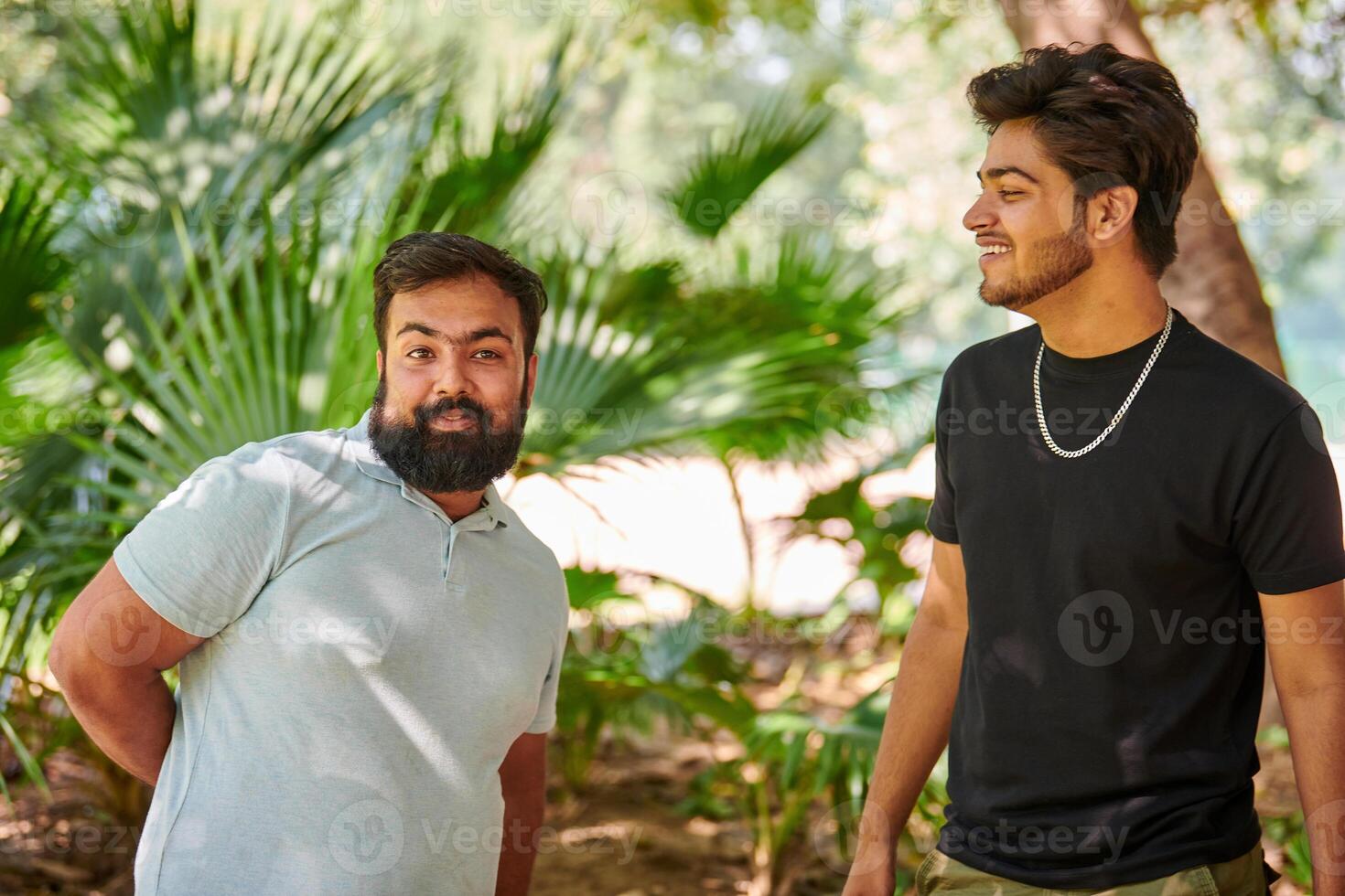 Two funny indian men laughing and speak Hindi in public park green palm leaves background photo