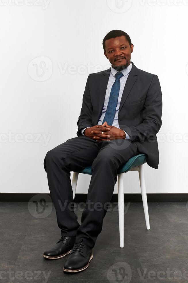 hombre negro afroamericano sonriente con traje de negocios sentado en una silla con los dedos cruzados foto